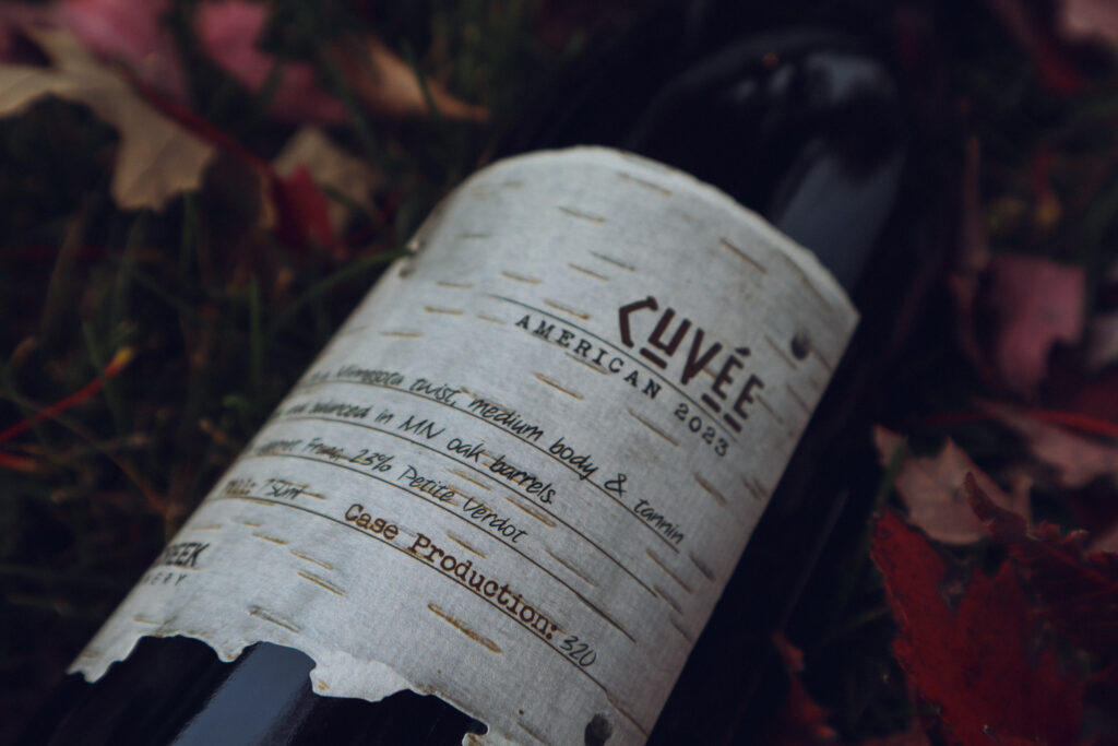 a bottle of cuvee wine rests on the ground